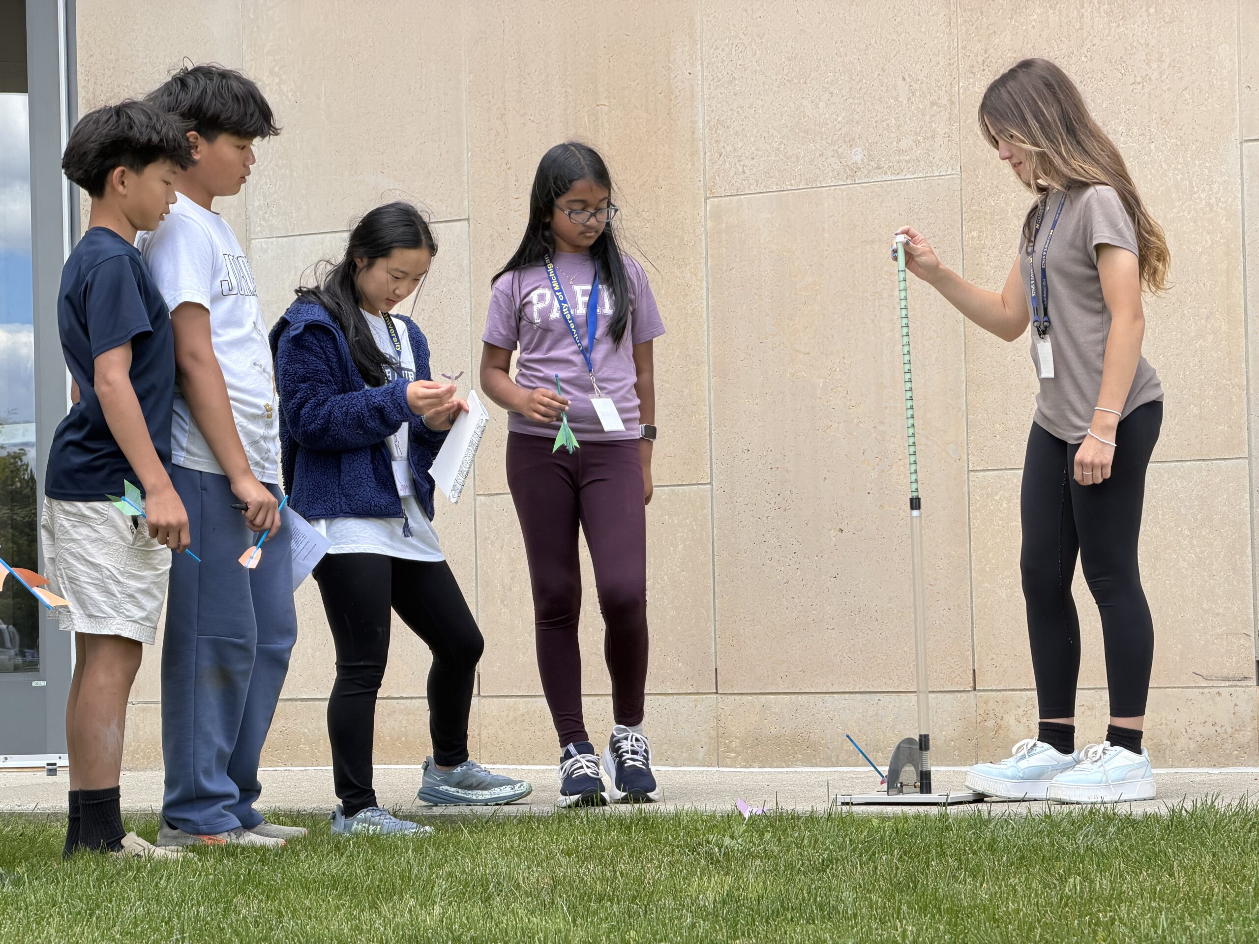 WISE GISE campers conduct a physics experiment outdoors, using a tall measuring device set up on the grass.