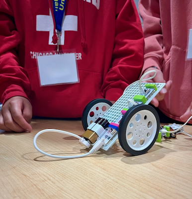 Close-up of a student's hands holding a small wheeled robot built during a WISE robotics camp.