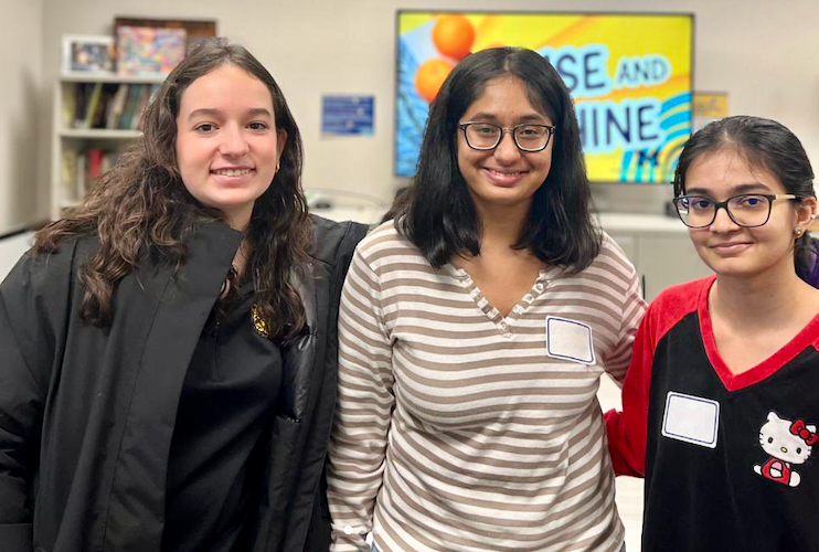 Three WISE college students smile together indoors, with a screen behind them displaying a "WISE & Shine" graphic.